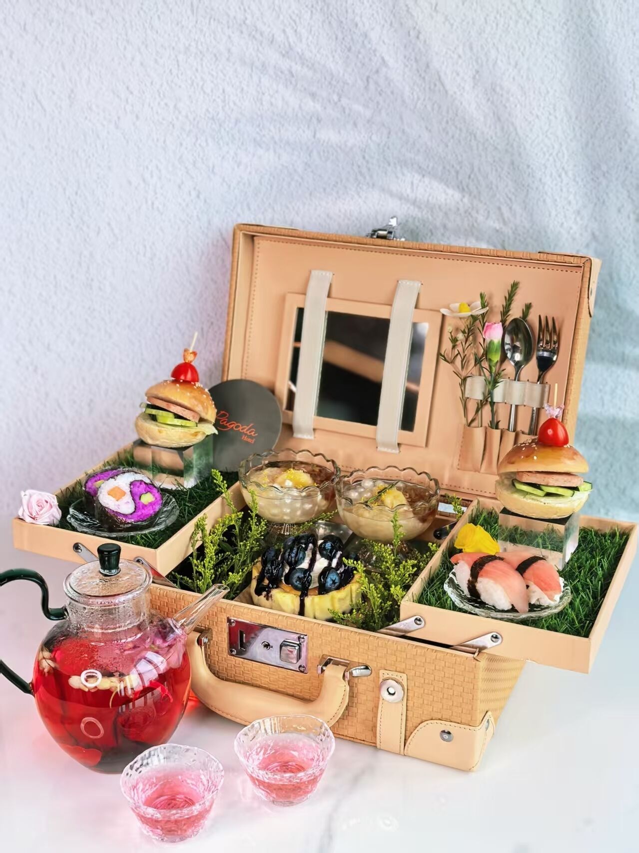A wooden box with compartments containing various food items, a glass teapot, and a small table with a teapot and cups.
