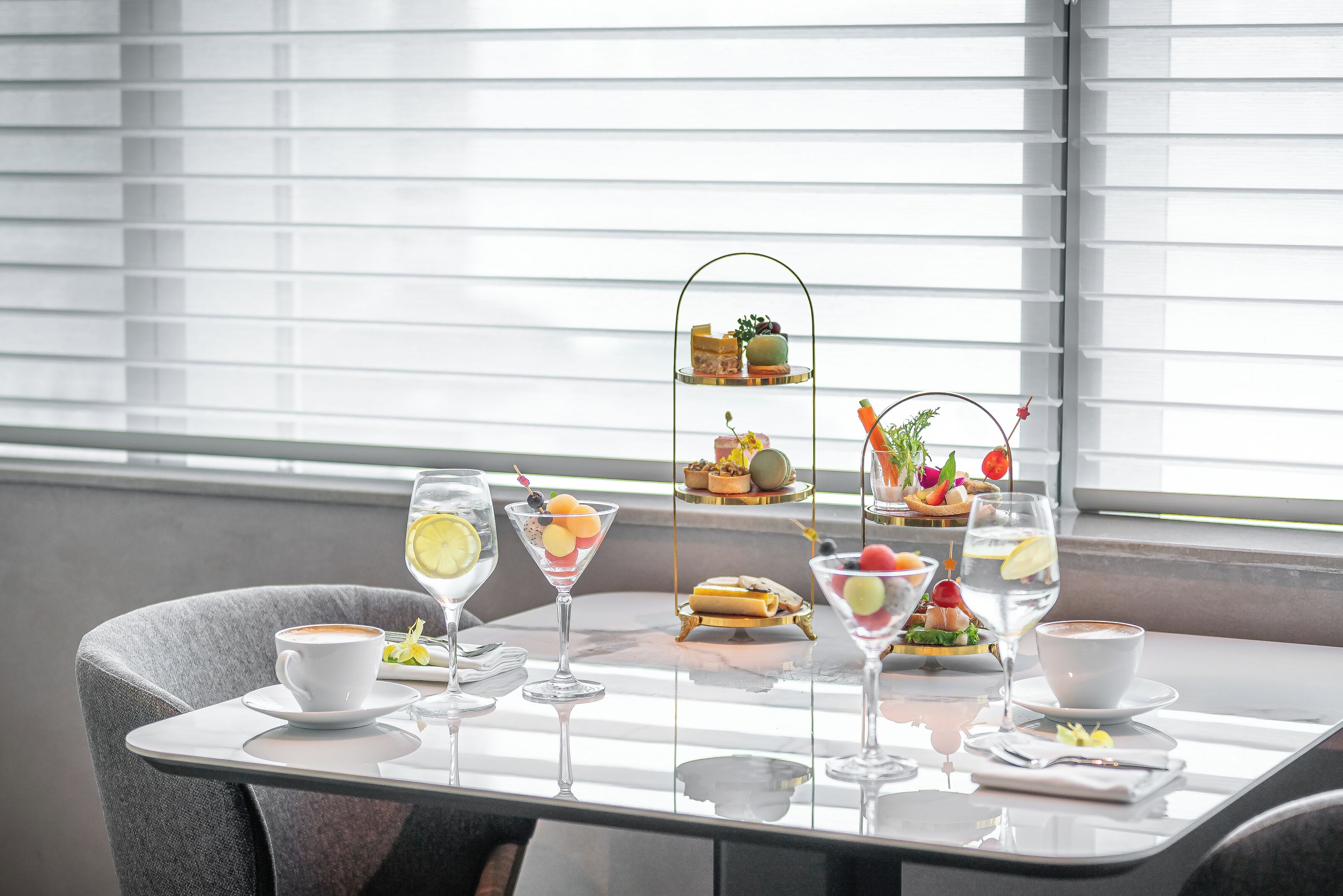 A dining table with a variety of food and drinks, including a tiered dessert stand, a glass of water, and a cup of coffee.