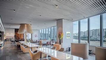 A modern hotel lobby with a large open space, seating areas, and a view of a cityscape through large windows.
