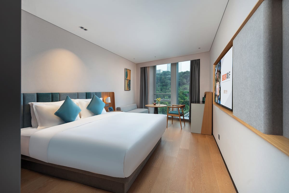 Una habitación de hotel moderna con una cama grande, una mesita y vistas al exterior.