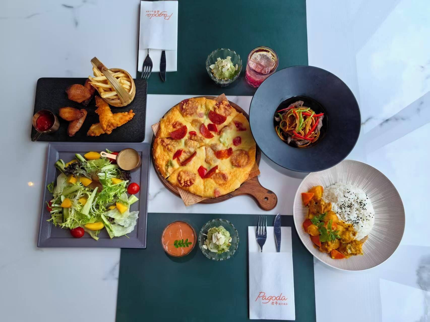 A variety of dishes including a pizza, salad, and rice bowl, arranged on a table with a placemat.