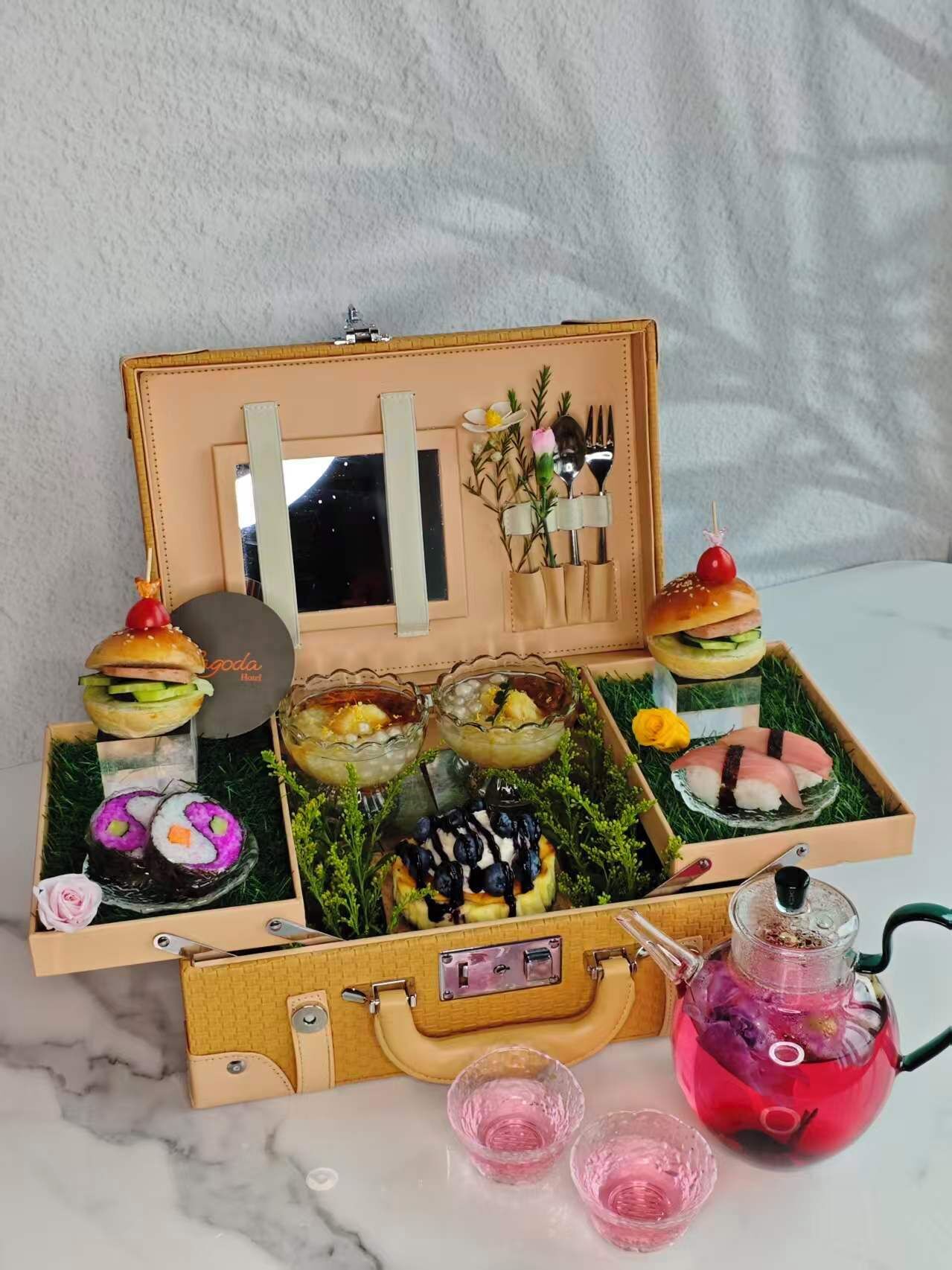 Presentación de comida con sushi, una hamburguesa y postres en una caja de madera con espejo y utensilios.
