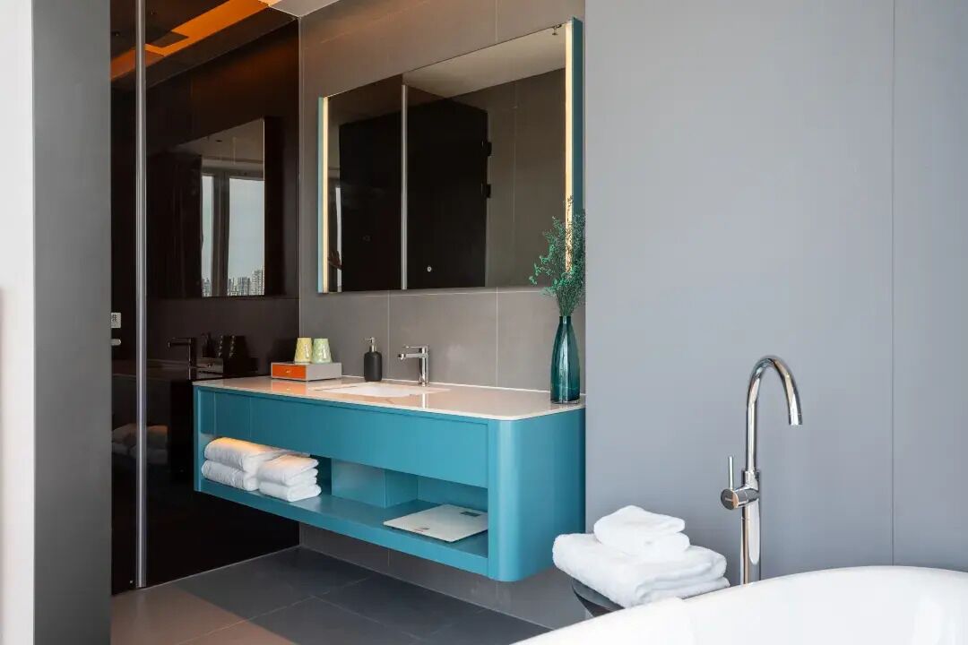 A modern bathroom with a large mirror, a blue vanity, a bathtub, and a glass shower enclosure.