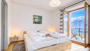 Ein Schlafzimmer mit einem Bett, einem Nachttisch, einer Lampe, einem Gemälde und Blick auf Berge vom Balkon aus.