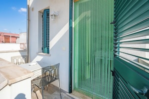 Een balkon met een tafel en stoelen, een groene deur en een raam met luiken.