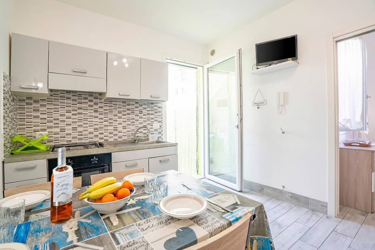 Una cocina moderna con armarios blancos, salpicadero de azulejos, una mesa de comedor preparada con platos, una botella y fruta.