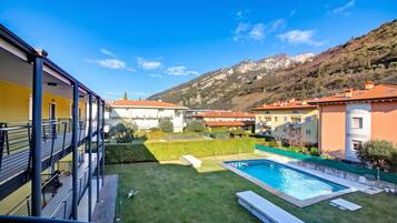 A residential building with a swimming pool, a grassy yard, and a mountain backdrop.