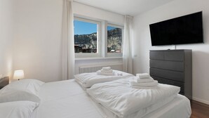Habitación de hotel con una cama grande, televisión de pantalla plana, cómoda y ventana con vista a la montaña.
