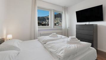 A hotel room with a large bed, a flat-screen TV, a dresser, and a window with a mountain view.