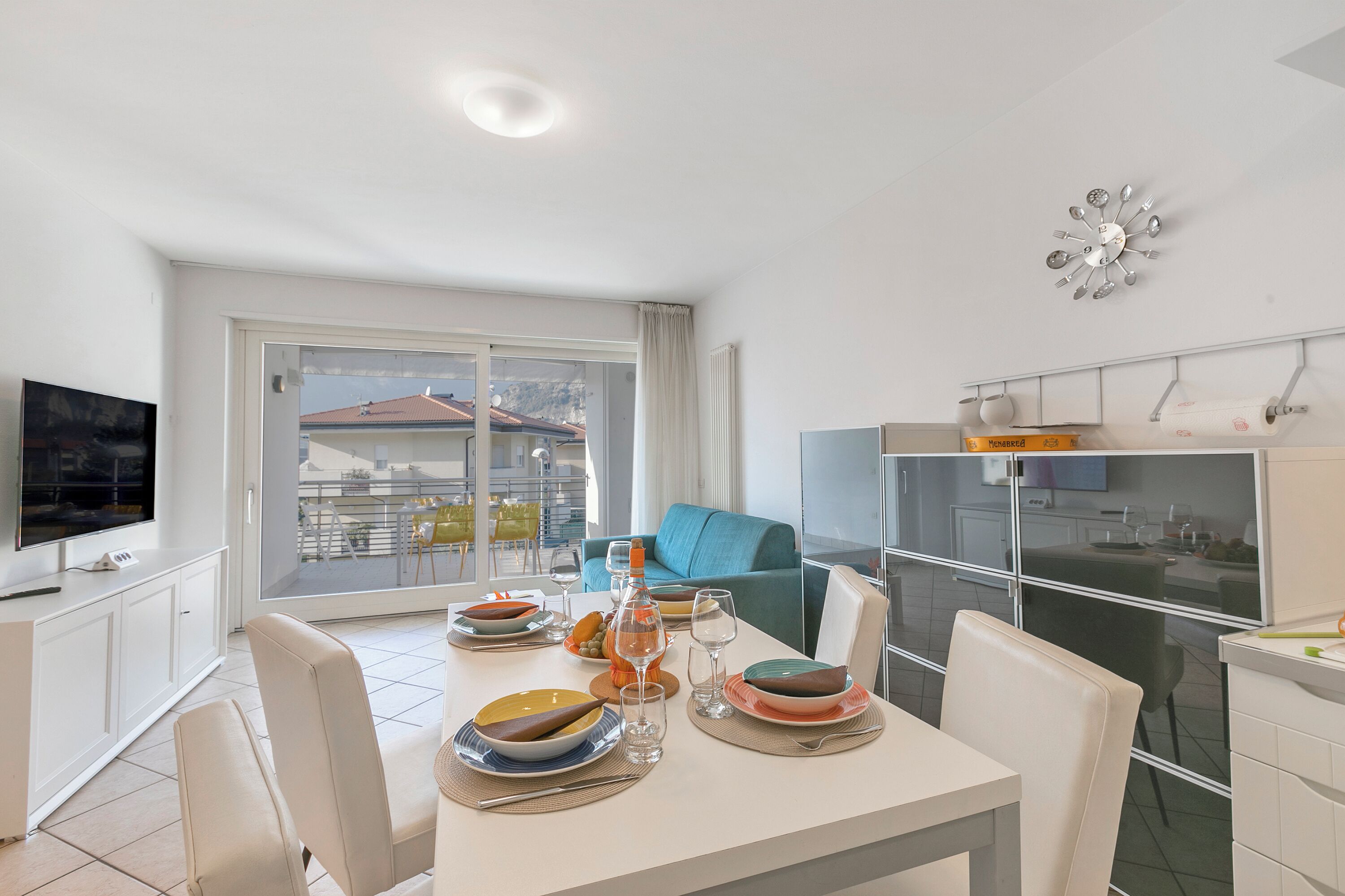 A modern dining area with a table set for four, a television, and a balcony with a view of buildings.