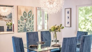 A dining area with a glass table, blue upholstered chairs, and a chandelier. - Unparalleled Views, Sauna, Hot Tub, Fire Pit, Game Room | Panorama by AvantStay (Sevierville)
