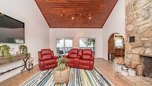 A spacious living room with a high ceiling, leather sofas, a large TV, and a stone fireplace. - Unparalleled Views, Sauna, Hot Tub, Fire Pit, Game Room | Panorama by AvantStay (Sevierville)