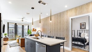A modern kitchen with a large island, a dining area with a black metal table, and a bedroom with a black metal bed frame. - Pool + Gym Access | Walk to Centennial Park | West End | Outlaw's Den (Nashville)
