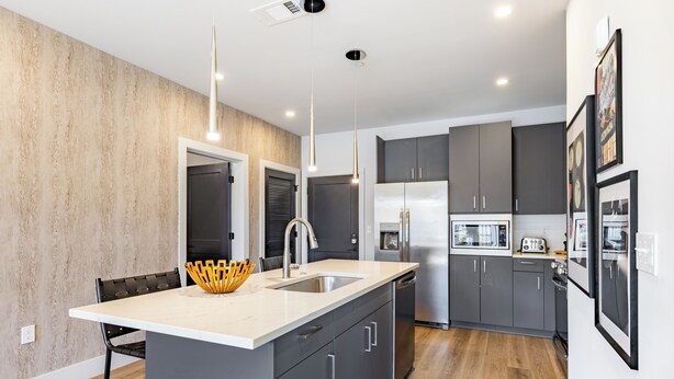 A modern kitchen with a central island, grey cabinets, stainless steel appliances, and pendant lighting. - Pool + Gym Access | Walk to Centennial Park | West End | Outlaw's Den (Nashville)