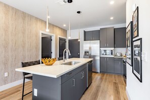 A modern kitchen with a central island, grey cabinets, stainless steel appliances, and pendant lighting. - Pool + Gym Access | Walk to Centennial Park | West End | Outlaw's Den (Nashville)