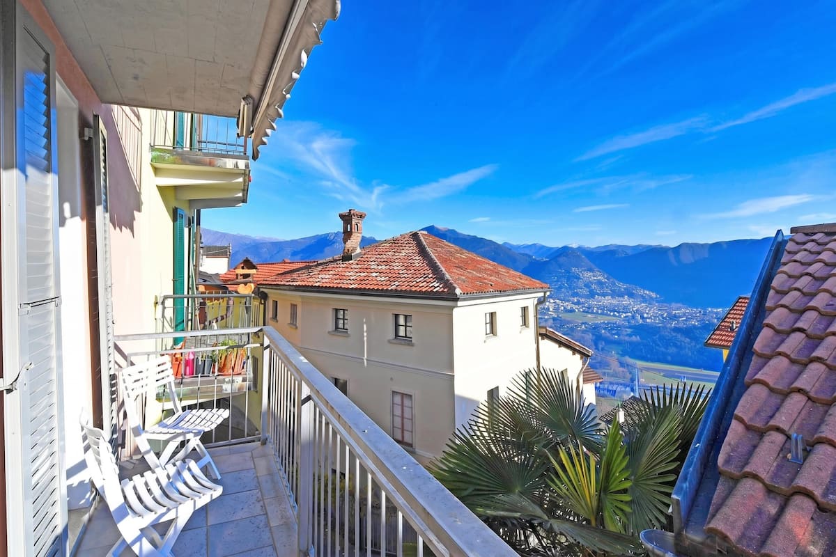 Un balcone con vista sulle montagne, un tetto in tegole e un edificio bianco.