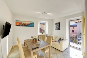 Un salon moderne comprenant un coin repas, un canapé, un téléviseur fixé au mur et un tableau représentant un paysage côtier.
