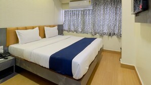 A hotel room with a bed, a ceiling fan, an air conditioning unit, a TV mounted on the wall, and a window with curtains. - hotel abraj inn  (Mumbai)