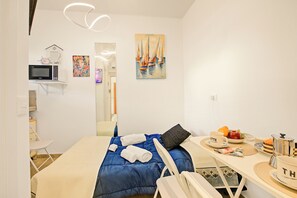 A hotel room with a bed, a desk with a laptop, a painting, and a breakfast setup.