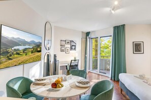A modern hotel room with a dining area, a bed, a large window with a view of the outdoors, and a flat-screen TV mounted on the wall. - La Perla Sul Lago (Paradiso)