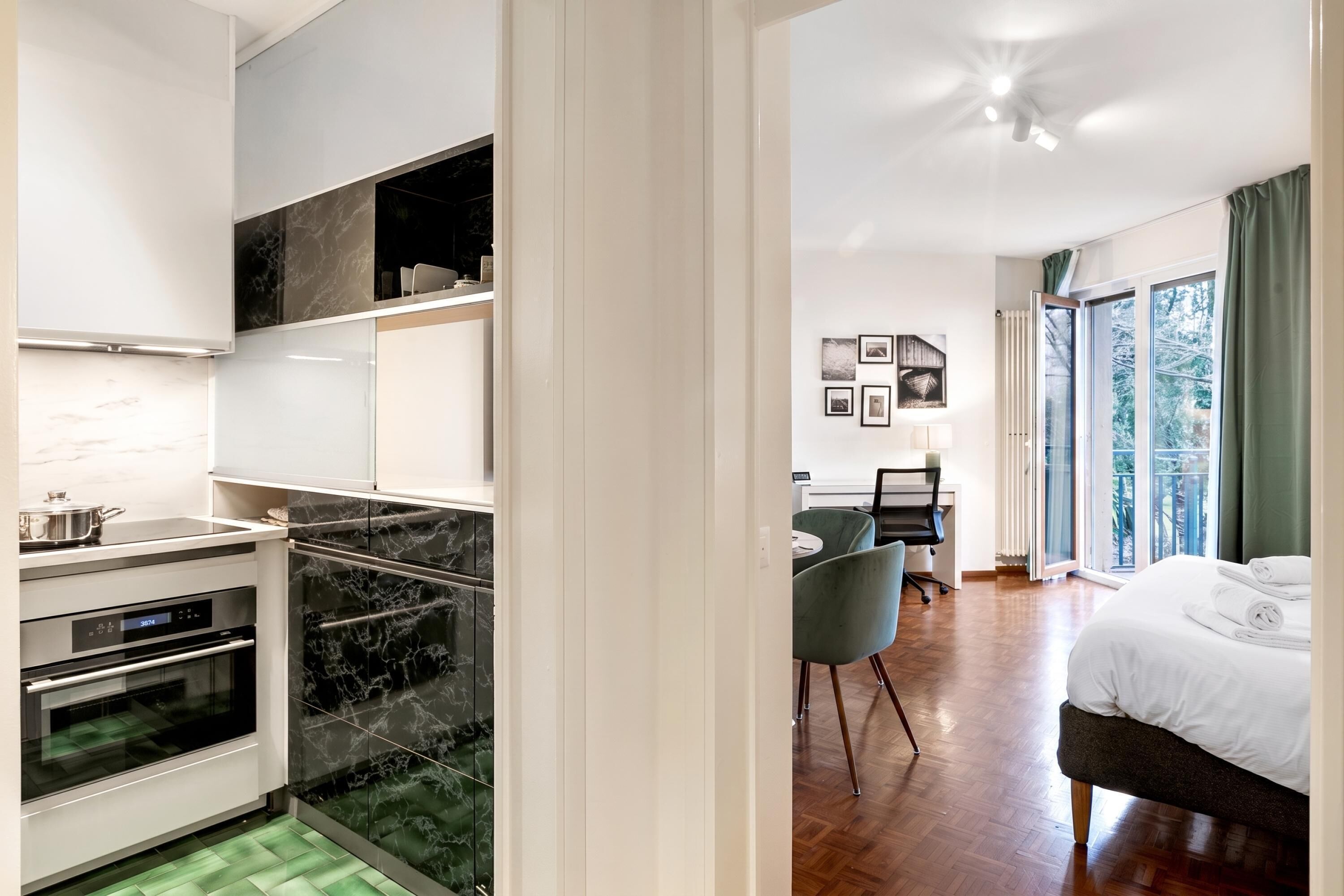 A modern hotel room with a kitchenette, a bed, a desk, and a view of the outdoors.