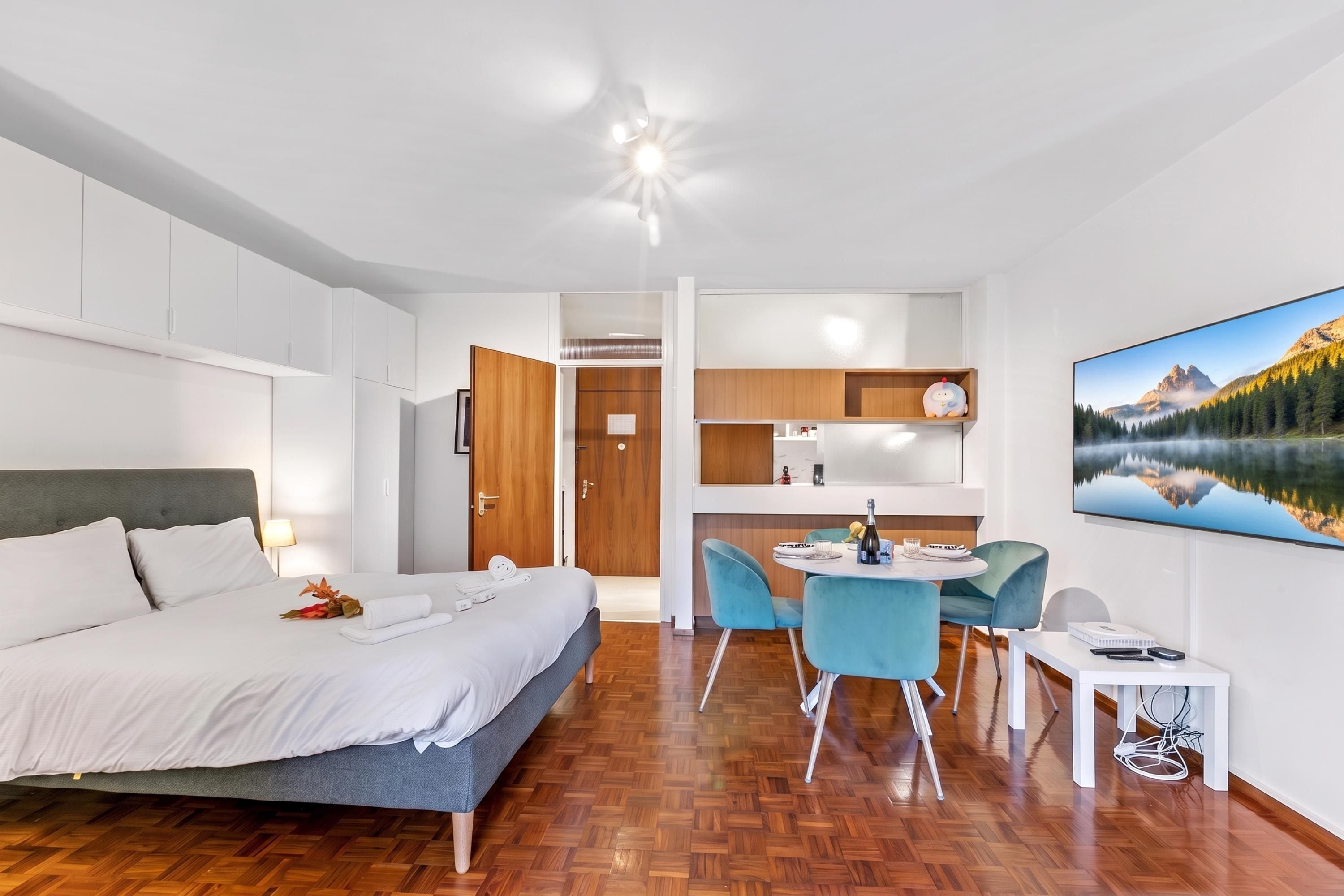 Una habitación de hotel moderna con una cama, un área de comedor con sillas, una mesita y un ventanal con vistas a la montaña.