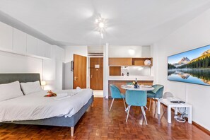 A modern hotel room with a bed, a dining area with chairs, a small table, and a large window with a mountain view.
