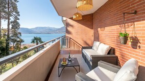 A balcony with wicker furniture, a table with a bottle and glasses, and a hanging plant. - La Perla Sul Lago - Studio With Balcony View (Paradiso)