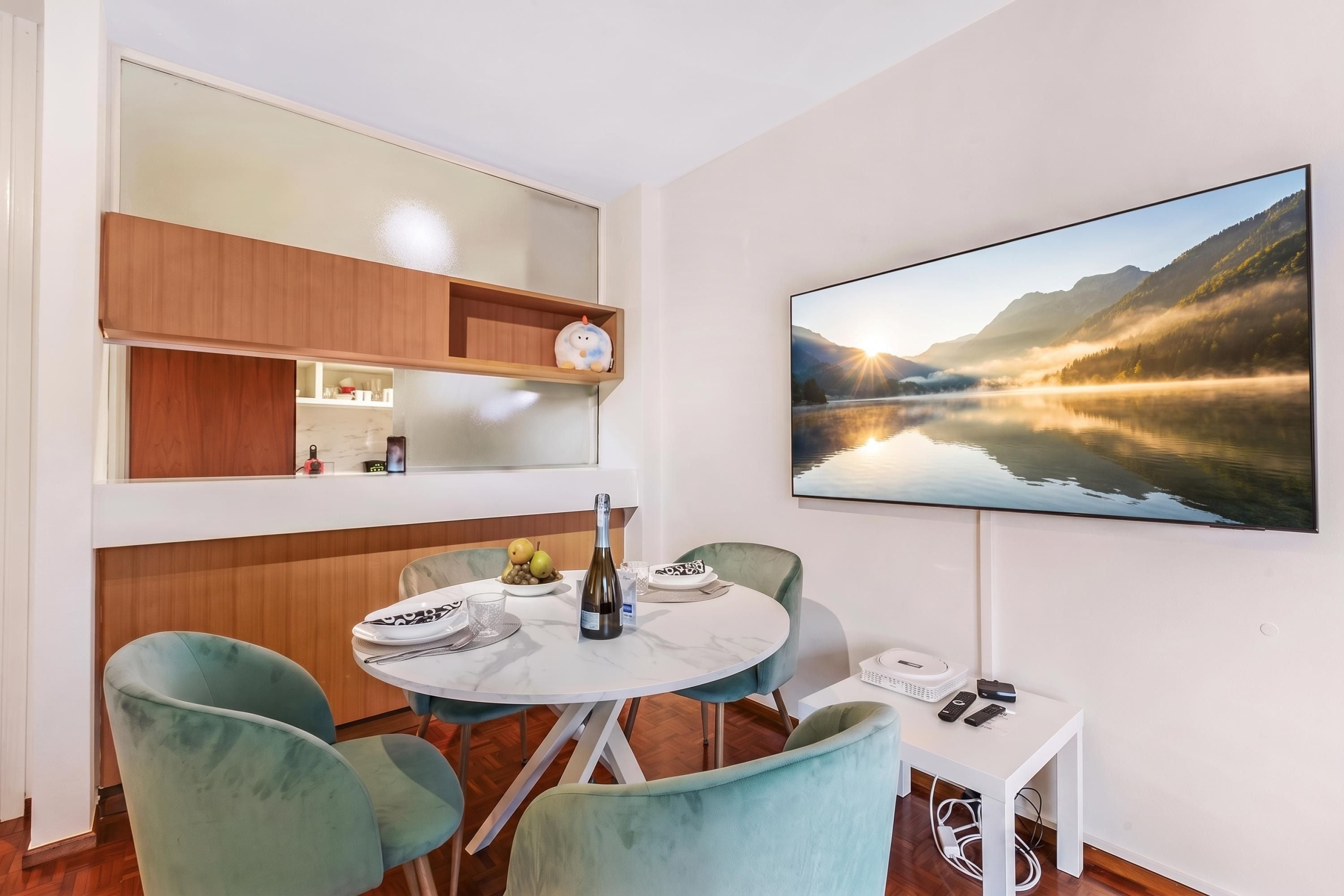 A modern dining area with a round table, two chairs, a bottle of wine, and a bowl of fruit.