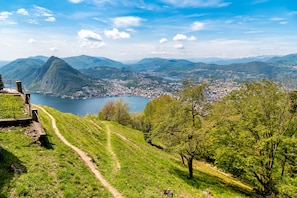 A scenic view of a mountainous landscape with a lake, a town in the valley, and a path leading to a viewing platform.