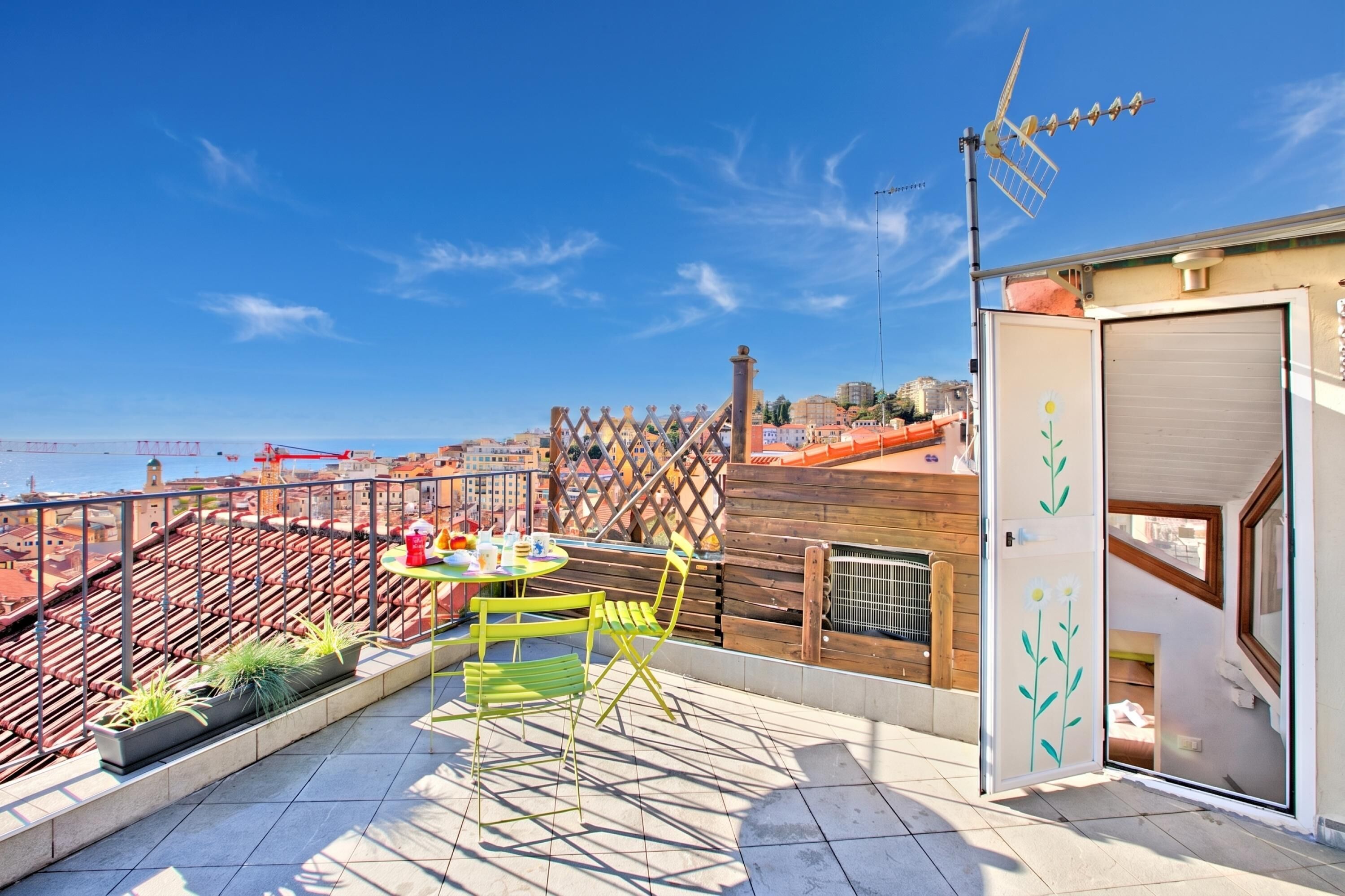 A rooftop terrace with a table and chairs, a view of the city, and a wooden fence.