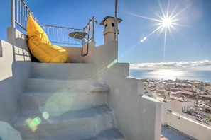 A staircase with a yellow cushion, a metal railing, and a view of the sea and town below.