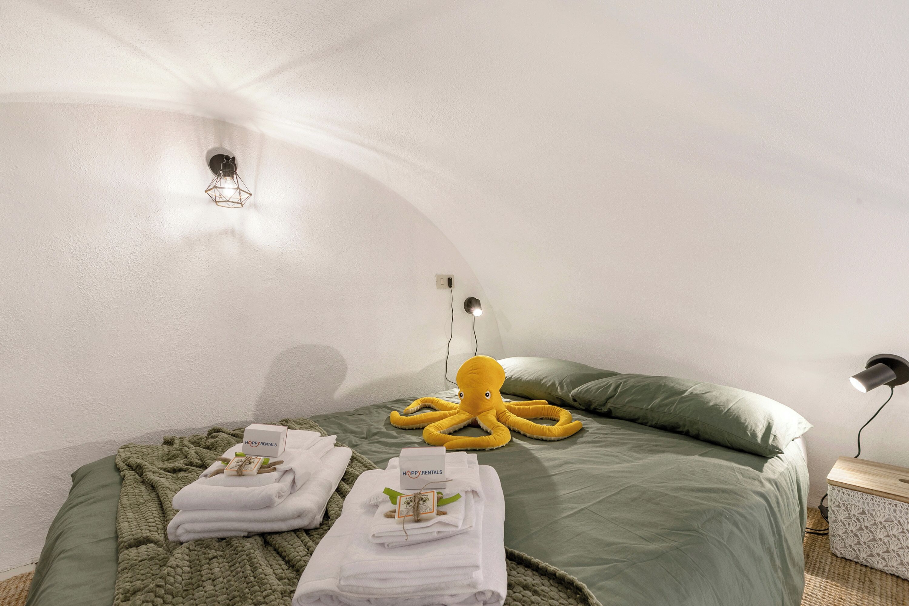 A room with a bed, a green blanket, a yellow octopus decoration, and a wall-mounted light fixture.