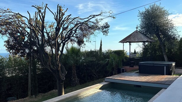 Ein Schwimmbecken mit Holzterrasse, umgeben von Bäumen und einem Pavillon.