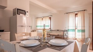 A dining area with a table set for two, a bottle of wine, and a bed in the background. - Relaxing Residence Baia dei Mirti Studio M3-3 persons-Unit 2 (Province of Sassari)
