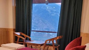 Habitación de hotel con cama, una mesa, dos sillas y vista a un paisaje montañoso a través de ventanas amplias.