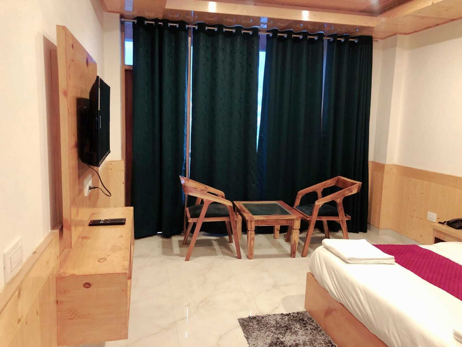 A hotel room with a bed, a desk with a chair, a TV mounted on the wall, and a window with curtains.