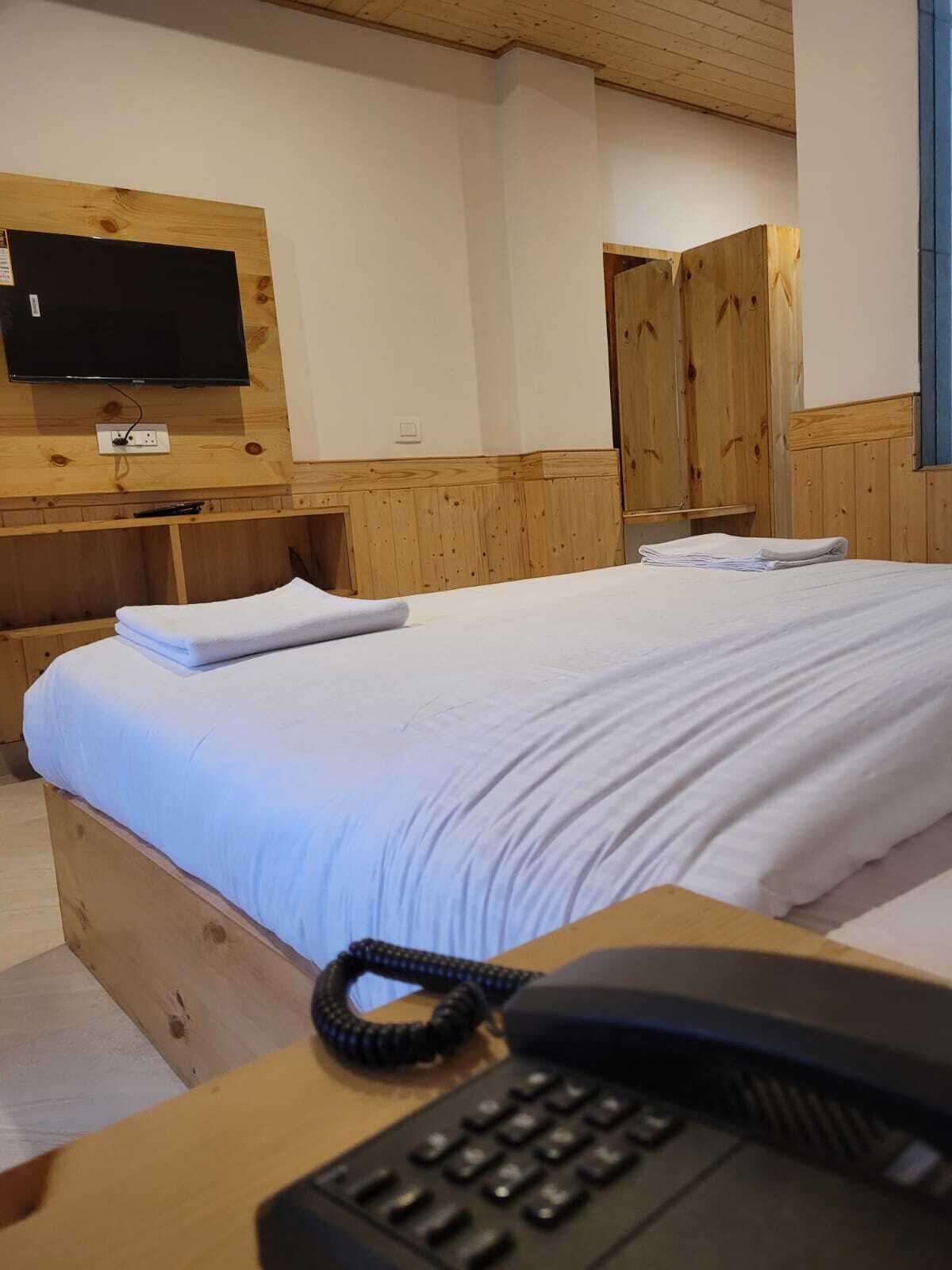 A hotel room with a bed, a desk with a telephone, a television mounted on the wall, and wooden wardrobes.
