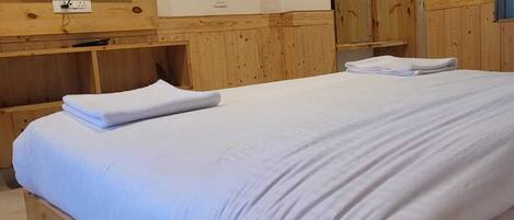 A hotel room with a bed, a desk with a telephone, a television mounted on the wall, and wooden wardrobes.