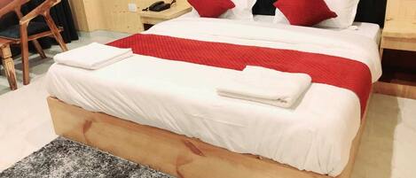 A neatly made bed with white and red bedding, a wooden headboard, and a small wooden nightstand with a phone.