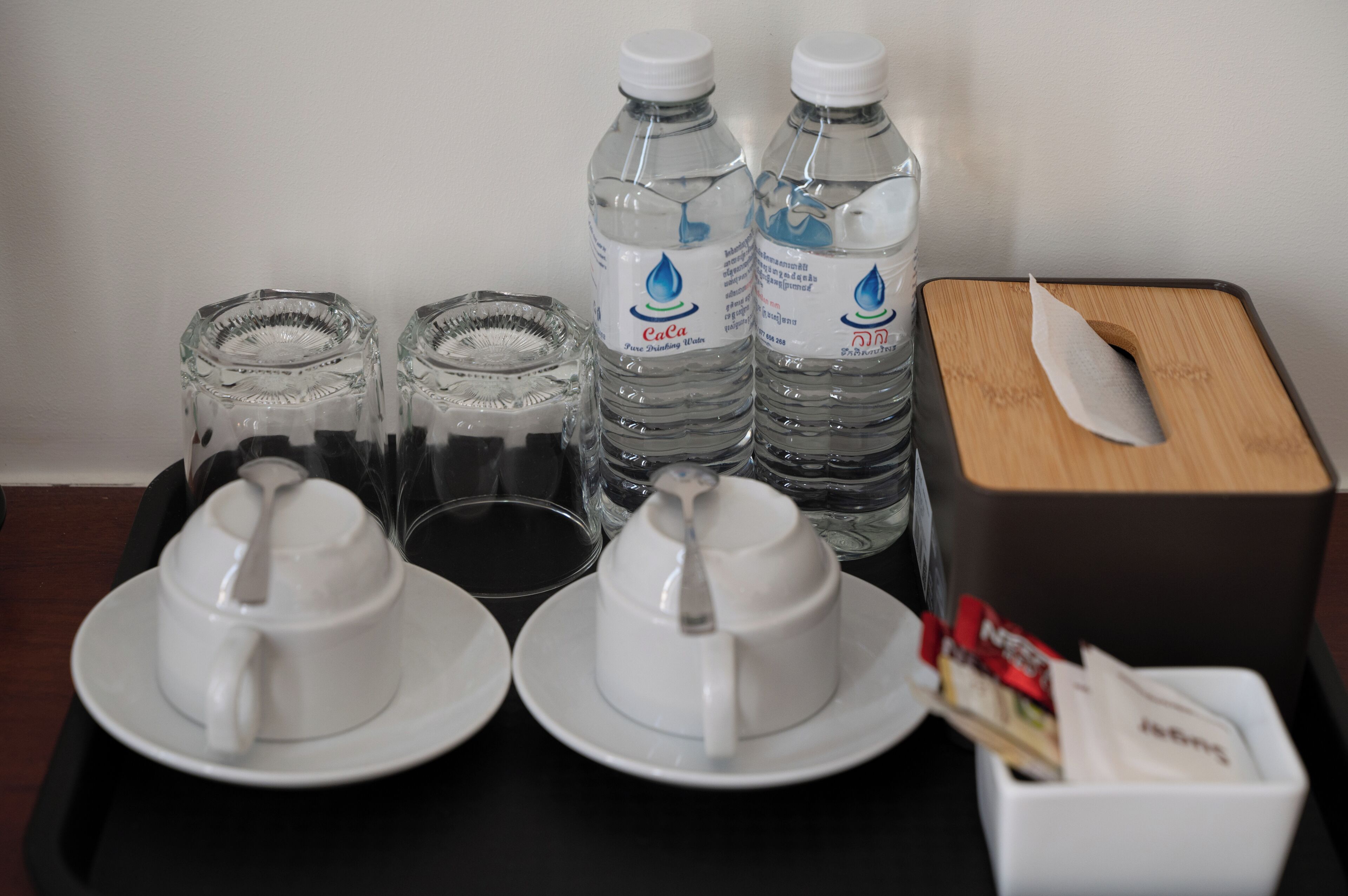 A table with two white cups, two water bottles, a tissue box, and a tray.