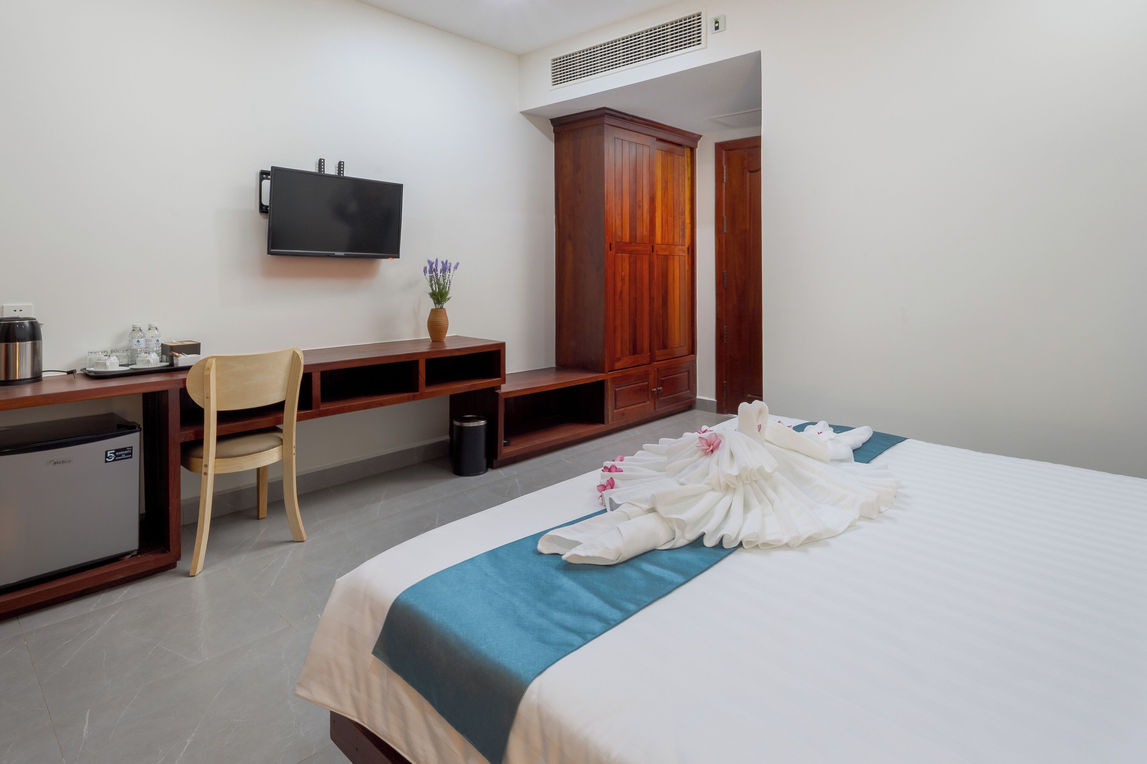 A hotel room with a bed, a desk, a chair, a TV, a wardrobe, and a minibar.