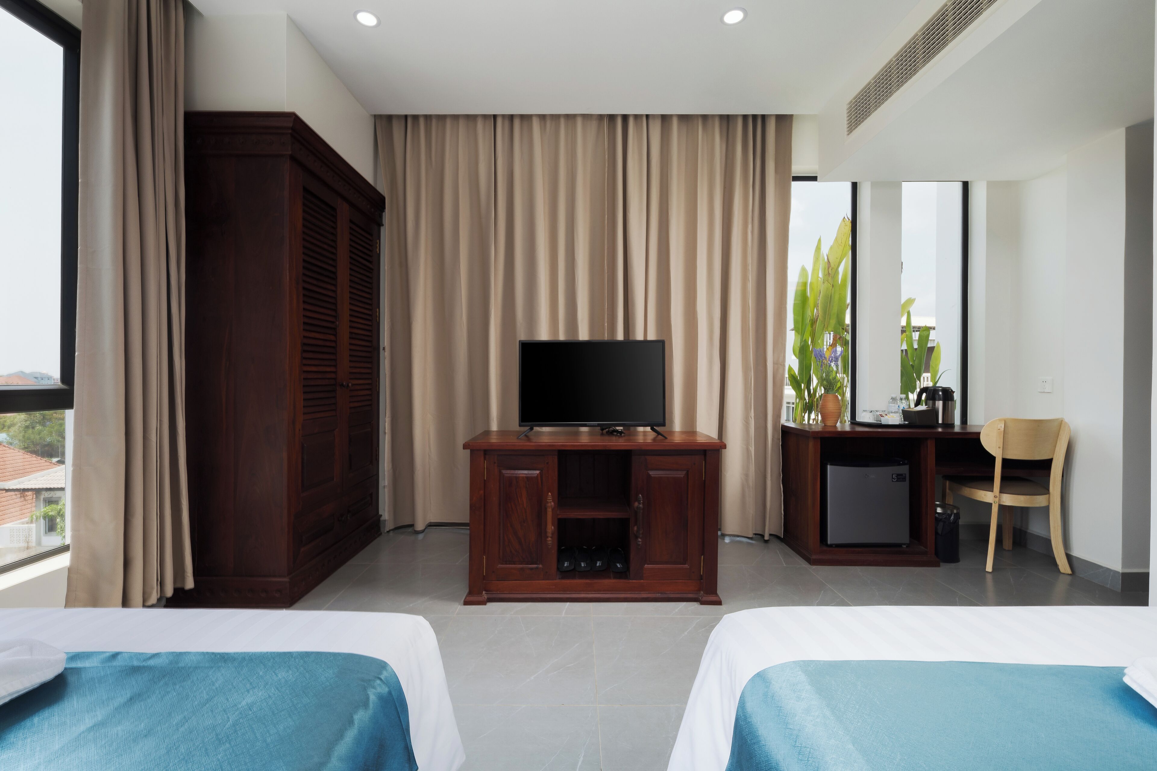A hotel room with two beds, a TV on a wooden cabinet, a desk with a chair, and a window with curtains.