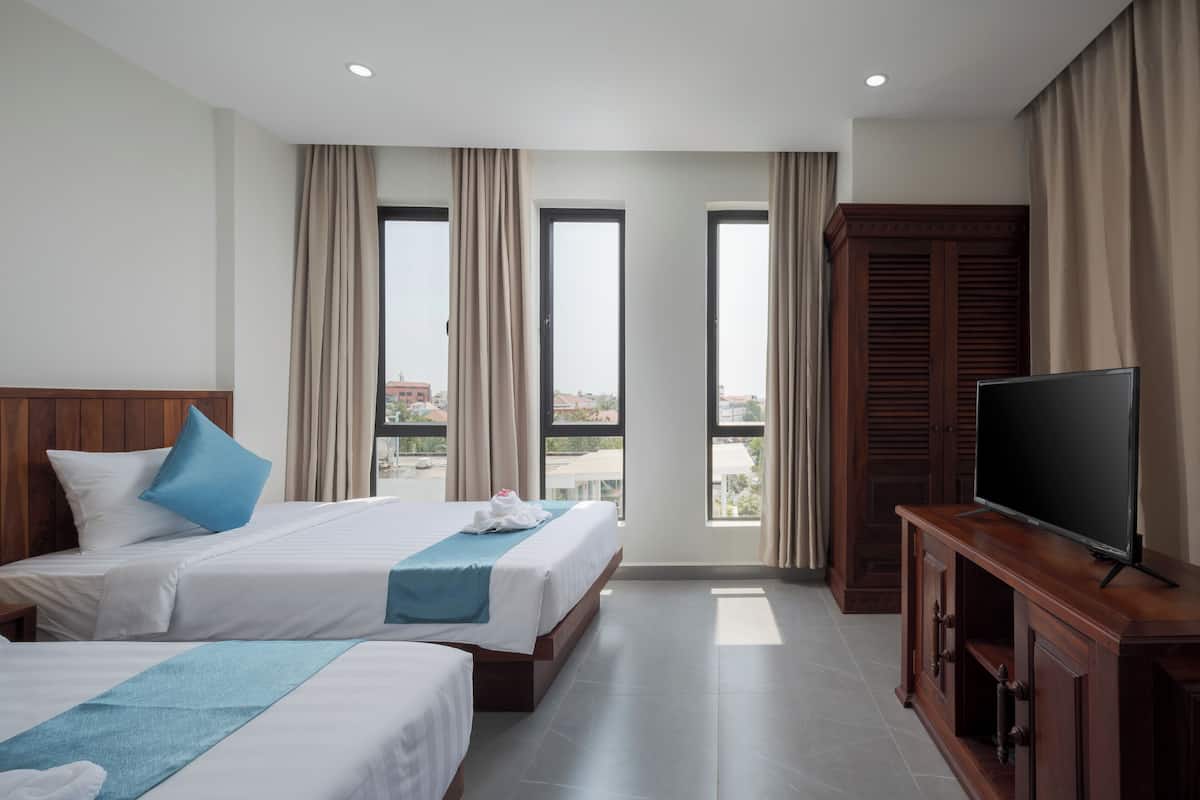 A hotel room with two beds, a TV, and a view of the city.