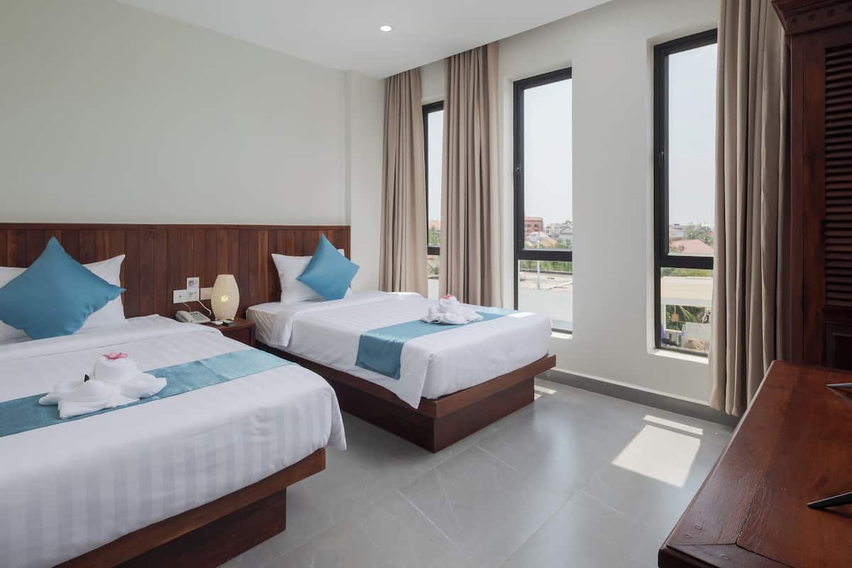 A hotel room with two beds, a wooden headboard, a desk, and large windows with curtains.