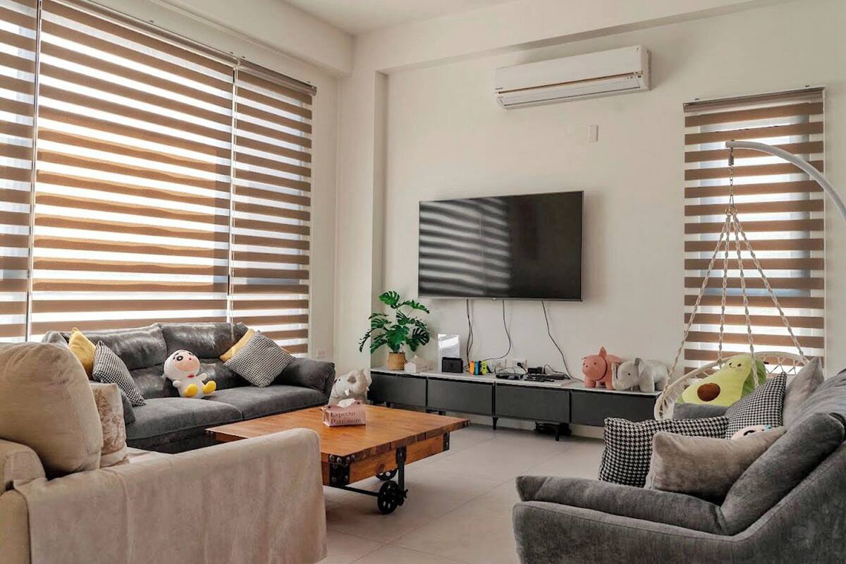 A modern living room with a grey sofa, a wooden coffee table, and a flat-screen TV mounted on the wall.