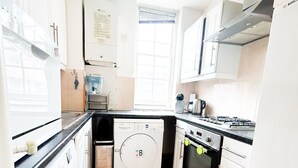 A compact kitchen with a washing machine, oven, and a window providing natural light. - Hammersmith 2 Bedroom Flat River Thames  (London)