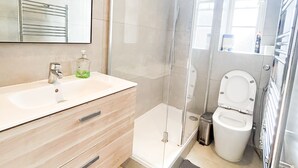 A modern bathroom with a glass shower enclosure, a toilet, and a sink with a mirror above it. - Hammersmith 2 Bedroom Flat River Thames  (London)