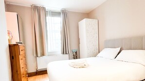 A bedroom with a large bed, a wardrobe, a dresser, and a window with curtains. - Hammersmith 2 Bedroom Flat River Thames  (London)