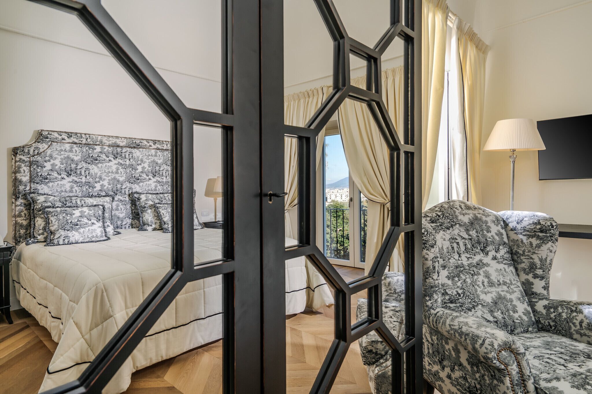 Une chambre avec un grand lit, une chaise, une table de chevet et une fenêtre avec des rideaux.